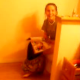 Some friends break into a bathroom to reveal their friend sitting on the toilet and trying to poop. The girl complains about her constipation.
